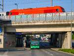 Graz. Diesel trifft auf Elektrohybrid: Am 20.06.2023 steht Wagen 184 der Graz Linien in der Haltestelle Don Bosco als Linie 32, darüber fährt in den gleichnamigen Bahnhof ein Wendezug nach Fehring ein.